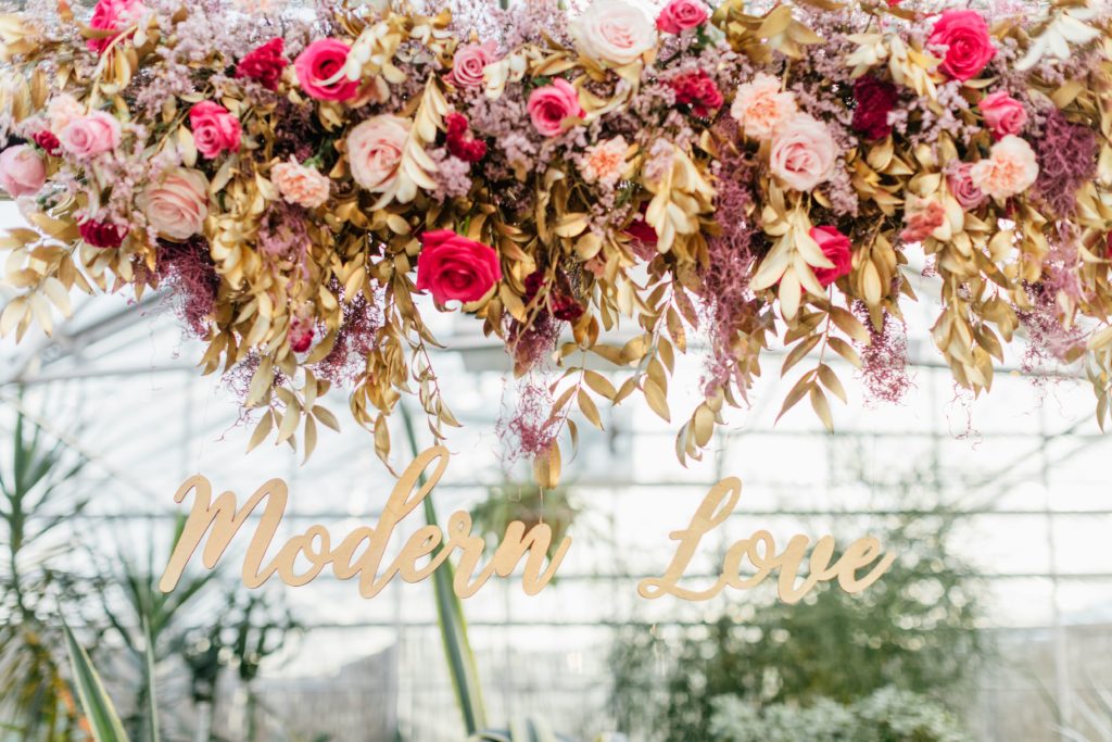 Love is in the Air styled shoot and bespoke bridal event at the Horticulture Center, custom hanging floral centerpiece in shades of pink, accented with gold painted foliage and featuring signage by EverLaser. Event design and florals by Sebesta Design. Photography by Emily Wren Photography. 