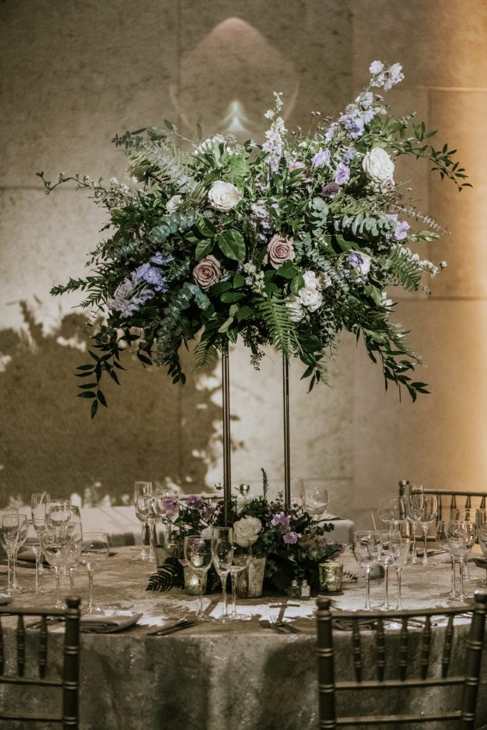 Winter wedding centerpiece featuring roses, larkspur, delphinium, fern, eucalyptus, jasmine vine and ruscus on tall metal stands with hanging candles at the Barnes Foundation. Photo by M2 Photography.