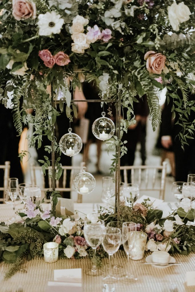 Winter wedding centerpiece featuring roses, larkspur, delphinium, fern, eucalyptus, jasmine vine and ruscus on tall metal stands with hanging candles at the Barnes Foundation by Sebesta Design. Photo by M2 Photography.