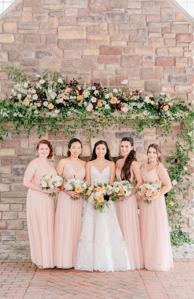 Bride & Bridesmaids standing in front of the fireplace embellished with flowers and foliage at the Ashford Estate by Sebesta Design. Photo by Emily Wren Photography.