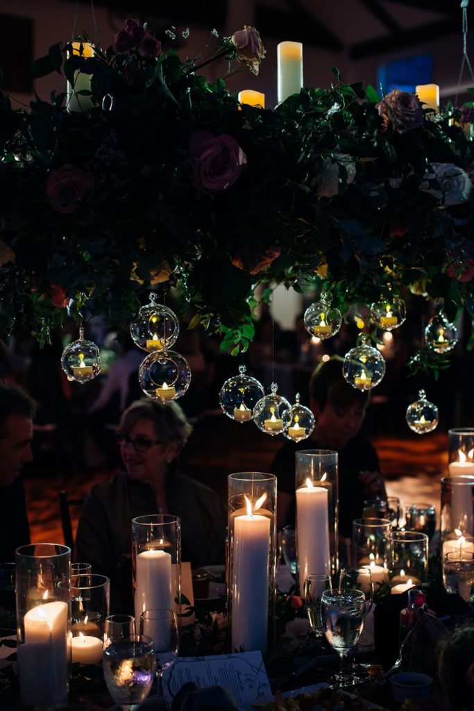 Candlelight glows from a hanging centerpiece framed by organic foliage and pillar candles by Sebesta Design at The Inn at Barley Sheaf Farm. Photo by Juliana Laury Photography