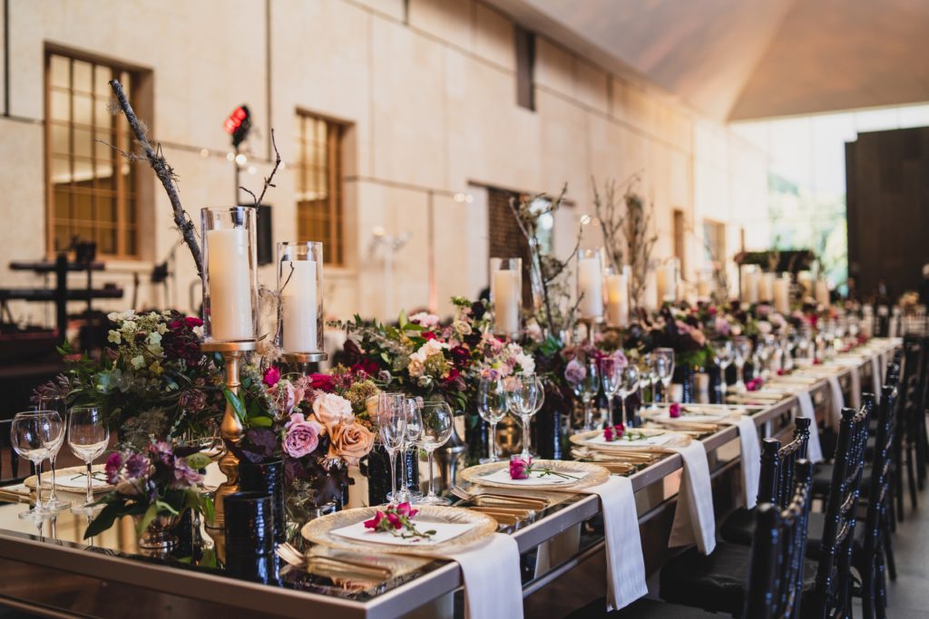 Striking Museum Wedding Reception long head table centerpiece design using multiple types of candles in varying heights, organic textural arrangements of flowers and foliage, including natural elements such as branches all down a mirrored table at the Barnes Foundation by Sebesta Design. Photography by Max Grudzinski Photography 