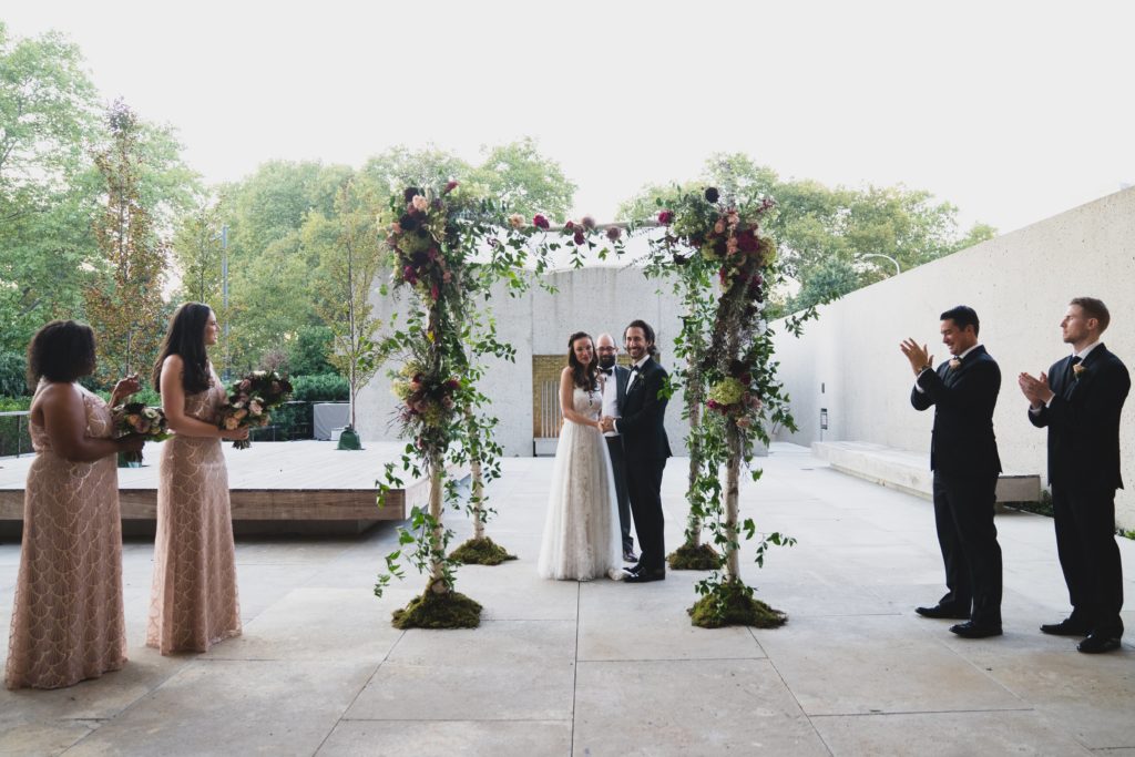 Lush Organic birch pole chuppah during modern organic museum wedding ceremony, covered in smilax vine and flowers, outdoor ceremony at the Barnes Foundation by Sebesta Design. Photography by Max Grudzinski Photography