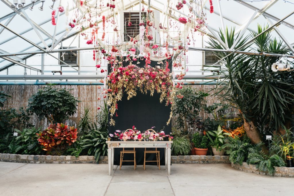 Love is in the Air styled shoot and bespoke bridal event at the Horticulture Center, beautiful sweetheart set up with luxe hanging florals in pink with accents of gold painted foliage, dramatic black backdrop and specialty mirrored table. Event design by Sebesta Design. Photography by Emily Wren Photography.