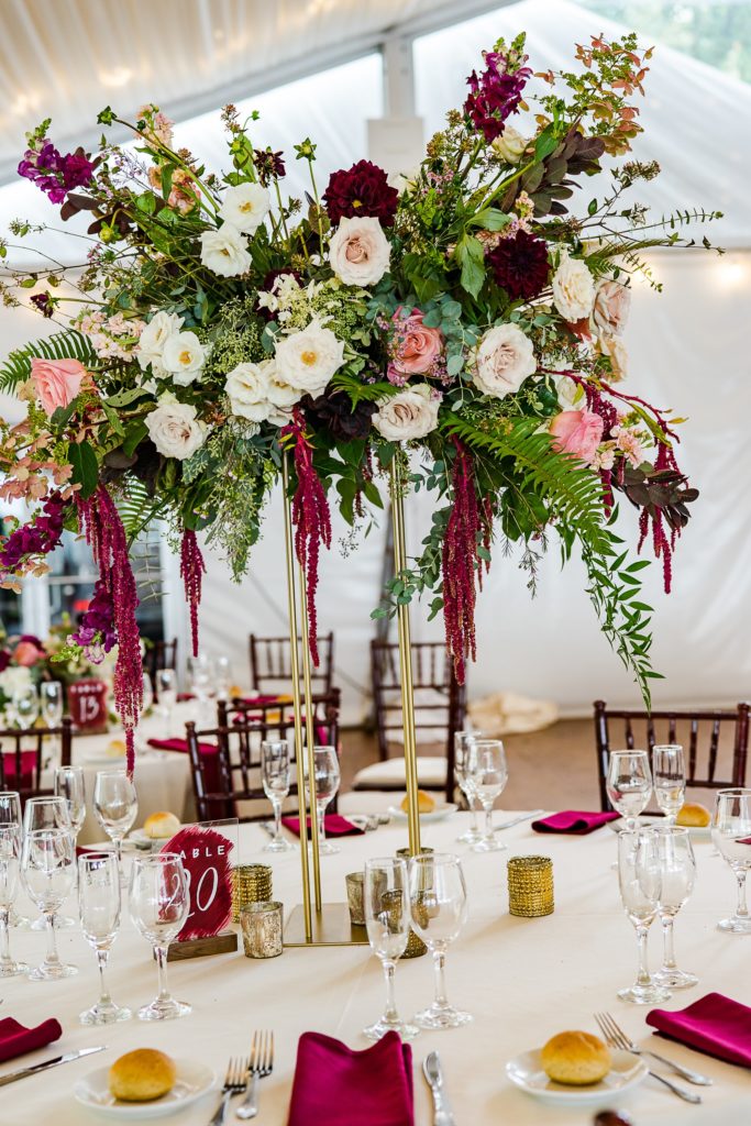 Bold Boho Organic Wedding Reception tall arrangement filled with texture and movement featuring plum branches, eucalyptus, fern, burgundy snapdragons, cranberry dahlias, tardiva hydrangea, waxflower, garden spray roses, garden roses, stock and dark cranberry hanging amaranthus at Glen Foerd on the Delaware designed by Sebesta Design and Photographed by The Caffeinated Photographer.